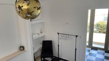 Ein Zimmer mit Schachbrettfußboden, einem schwarzen Stuhl, einem weißen Regal mit einer Uhr und einem Kleiderständer.