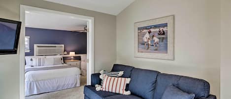 A bedroom with a bed, a gray couch, a painting, and a door leading to another room.