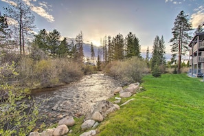 A river flowing through a grassy area with rocks, surrounded by trees and a building with a balcony. - Winter Park Condo on Bus Route, 2 Blocks to Dtwn! (Winter Park)