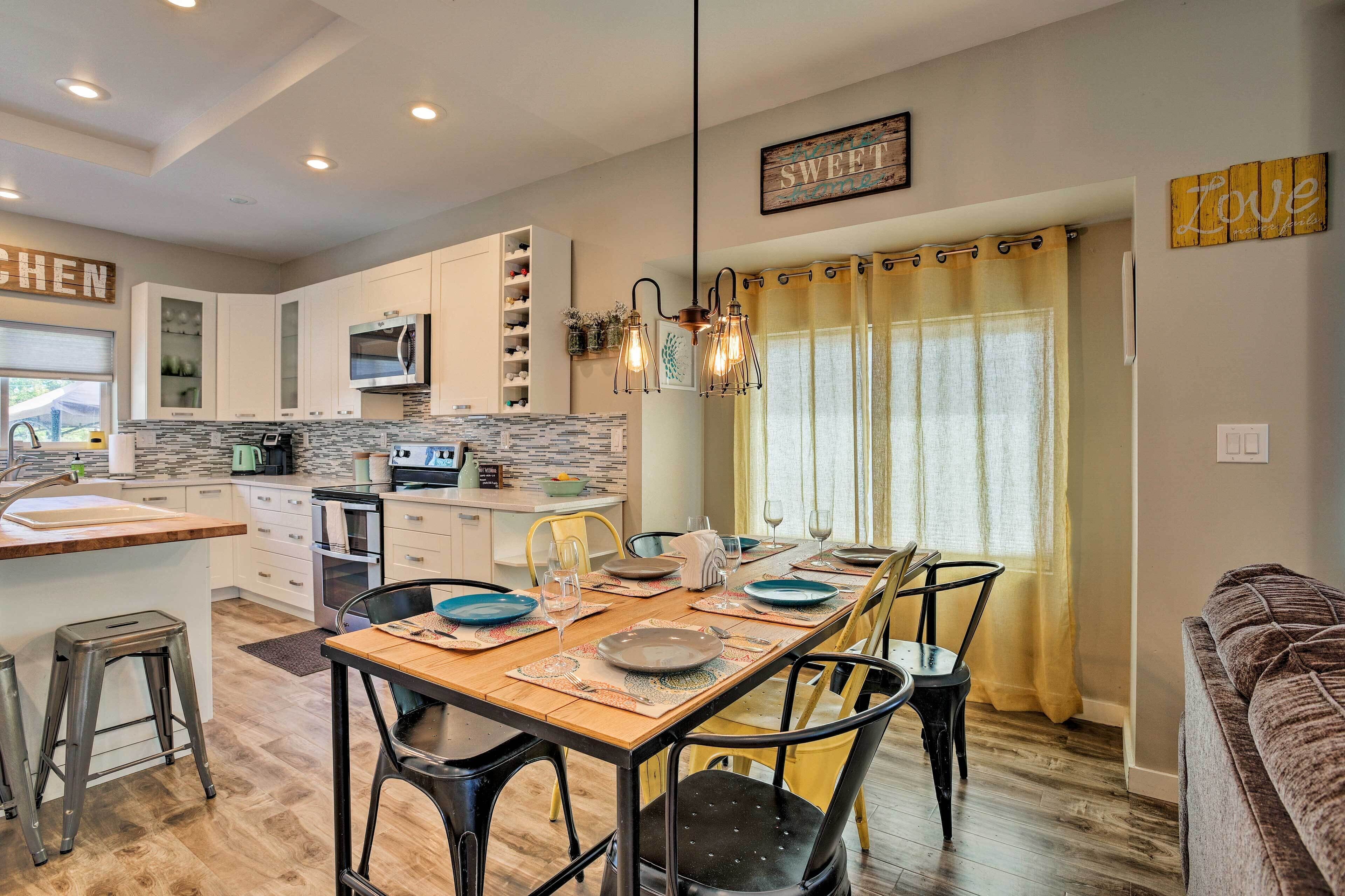 Una cocina moderna con armarios blancos, microondas integrado y un comedor con mesa y sillas de madera.