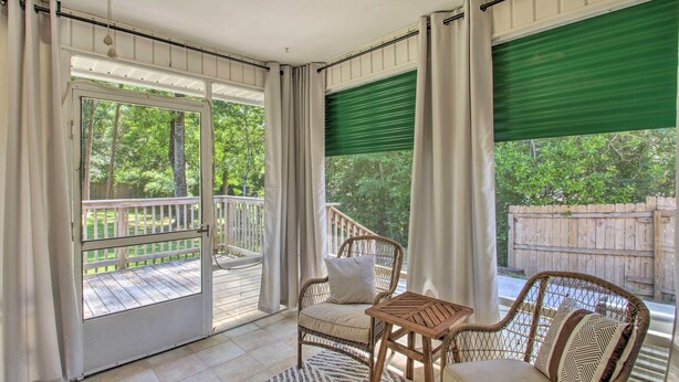A covered porch with wicker furniture, a view of a wooden deck, and a green roller shade. - Cozy-modern Pensacola Home: Large Yard, Grill (Pensacola)