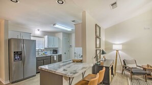 A modern kitchen with stainless steel appliances, a marble island, and a dining area with a table and chairs. - Cozy-modern Pensacola Home: Large Yard, Grill (Pensacola)