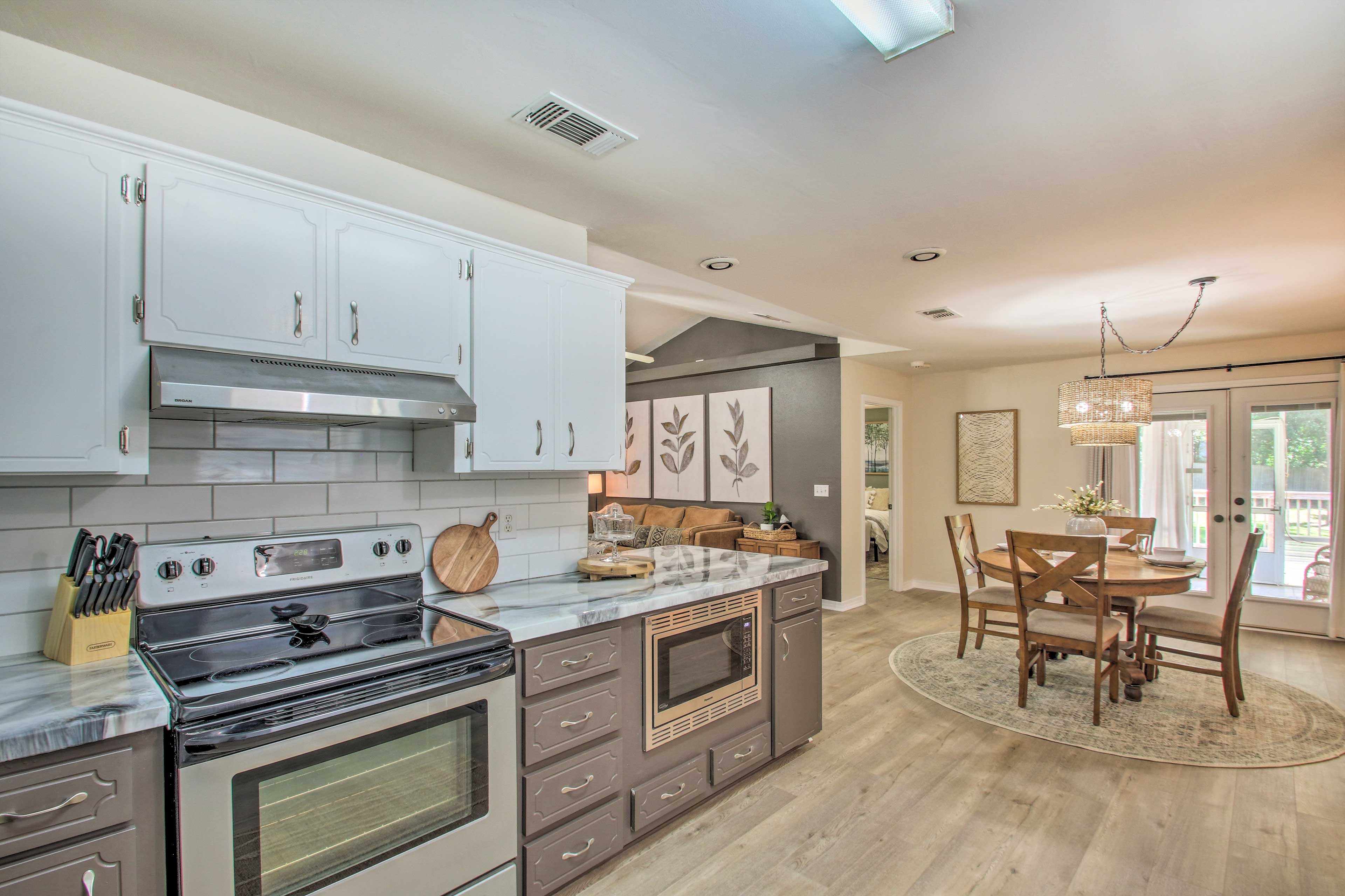 A modern kitchen with a central island, built-in oven, and microwave. There is a dining area with a table and chairs.