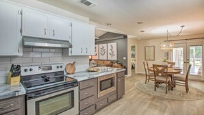 A modern kitchen with a central island, built-in oven, and microwave. There is a dining area with a table and chairs. - Cozy-modern Pensacola Home: Large Yard, Grill (Pensacola)
