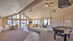 Un espace intérieur spacieux comprenant une table de billard, des sièges confortables et de grandes fenêtres laissant entrer la lumière naturelle.