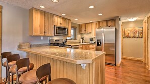 Une cuisine moderne avec des meubles en bois, un plan de travail en granit, des appareils électroménagers en acier inoxydable et un coin bar avec des tabourets.