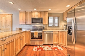 A modern kitchen with wooden cabinets, stainless steel appliances, and a patterned rug.