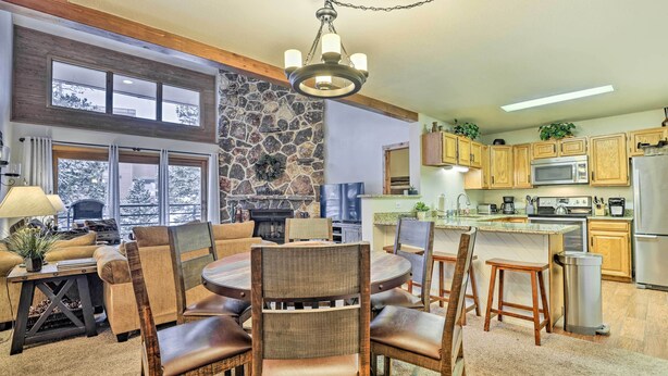 A cozy living room with a fireplace, a dining area with wicker furniture, and a kitchen with wooden cabinets and modern appliances. - All-season Resort Condo: 5 Mi to Dillon Reservoir (Silverthorne)