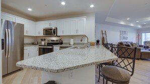 A modern kitchen with white cabinetry, a granite countertop, stainless steel appliances, and a dining area with a wooden table and chairs. - Water Views + Pool Access: Lake Ozark Escape! (Lake Ozark)
