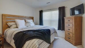 A bedroom with a bed, a wooden dresser, a television, and a window with blinds. - Water Views + Pool Access: Lake Ozark Escape! (Lake Ozark)