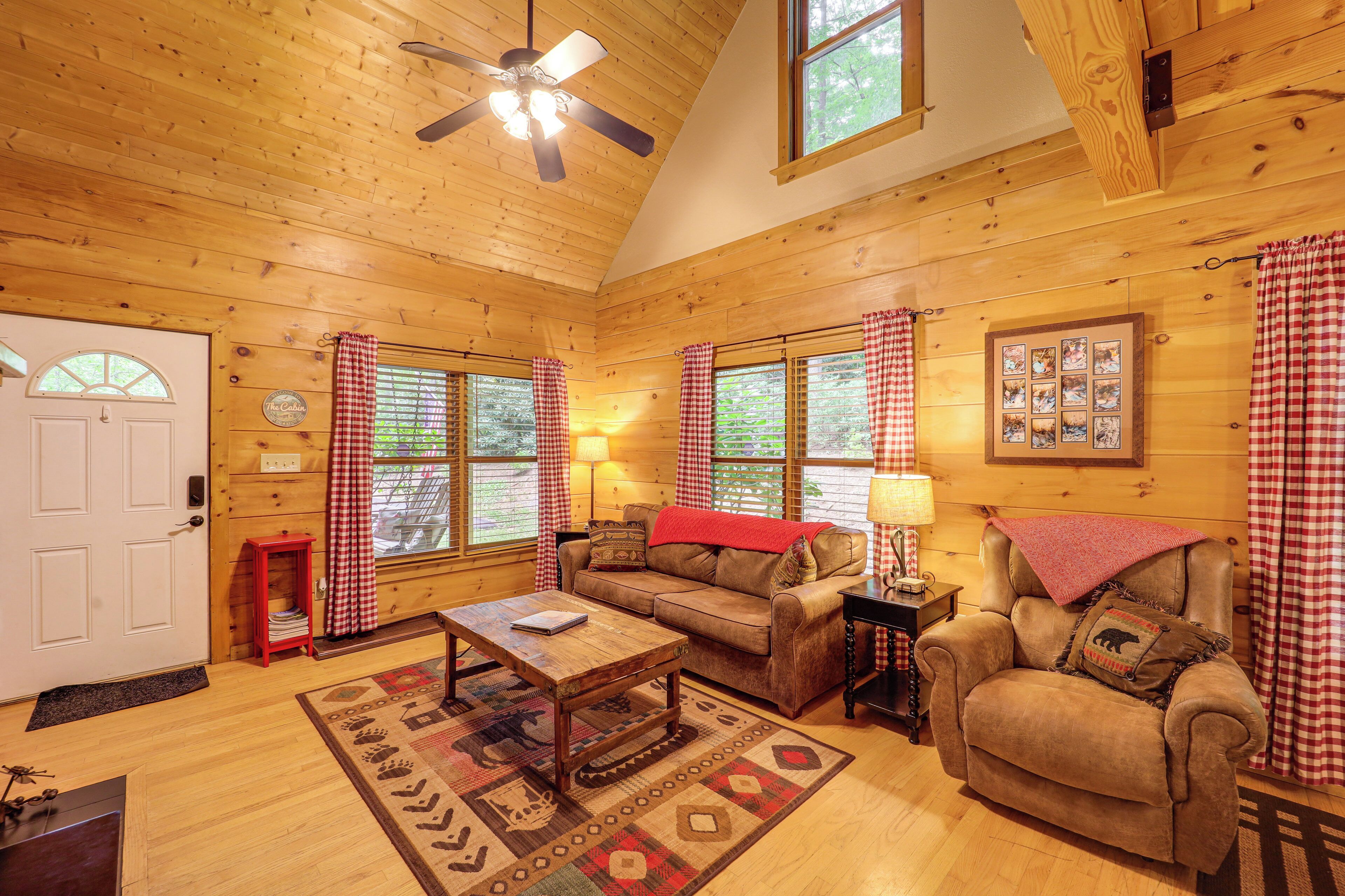 A cozy cabin interior with a wooden ceiling, a sofa, a chair, and a coffee table.