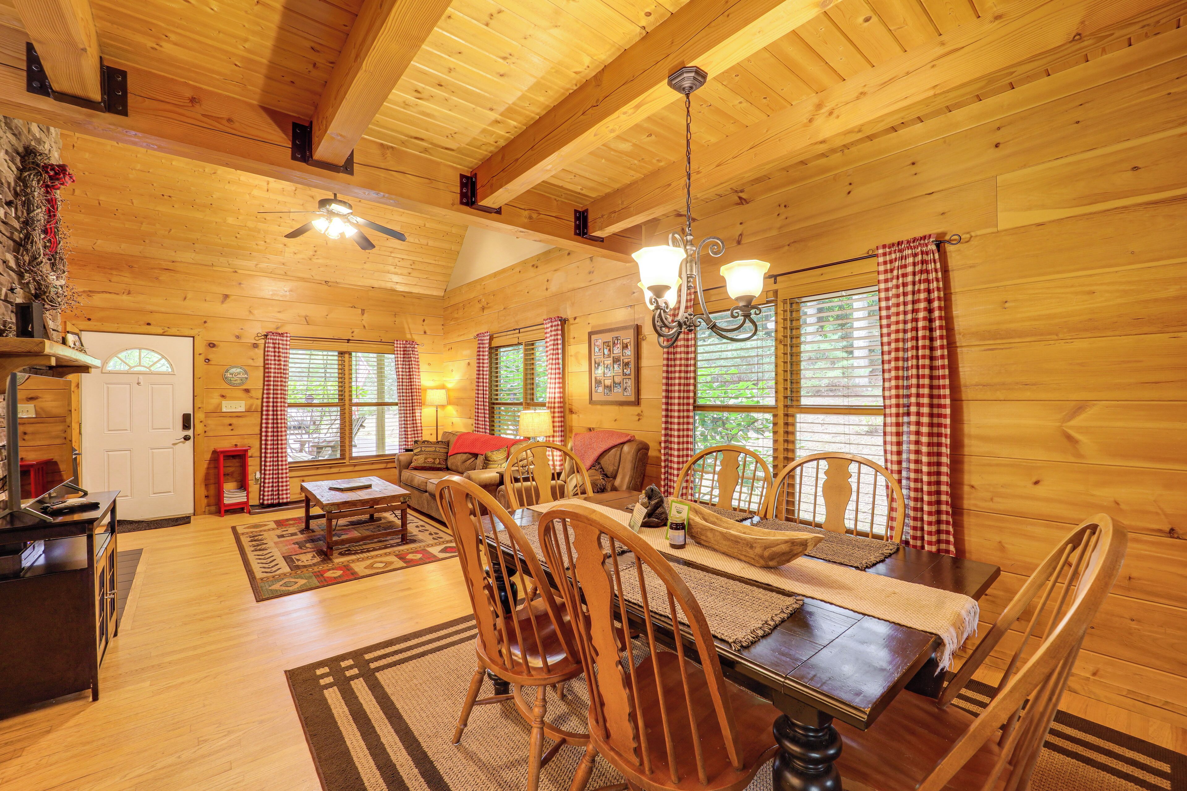 A wooden cabin interior with a dining area, kitchen, and a ceiling fan.