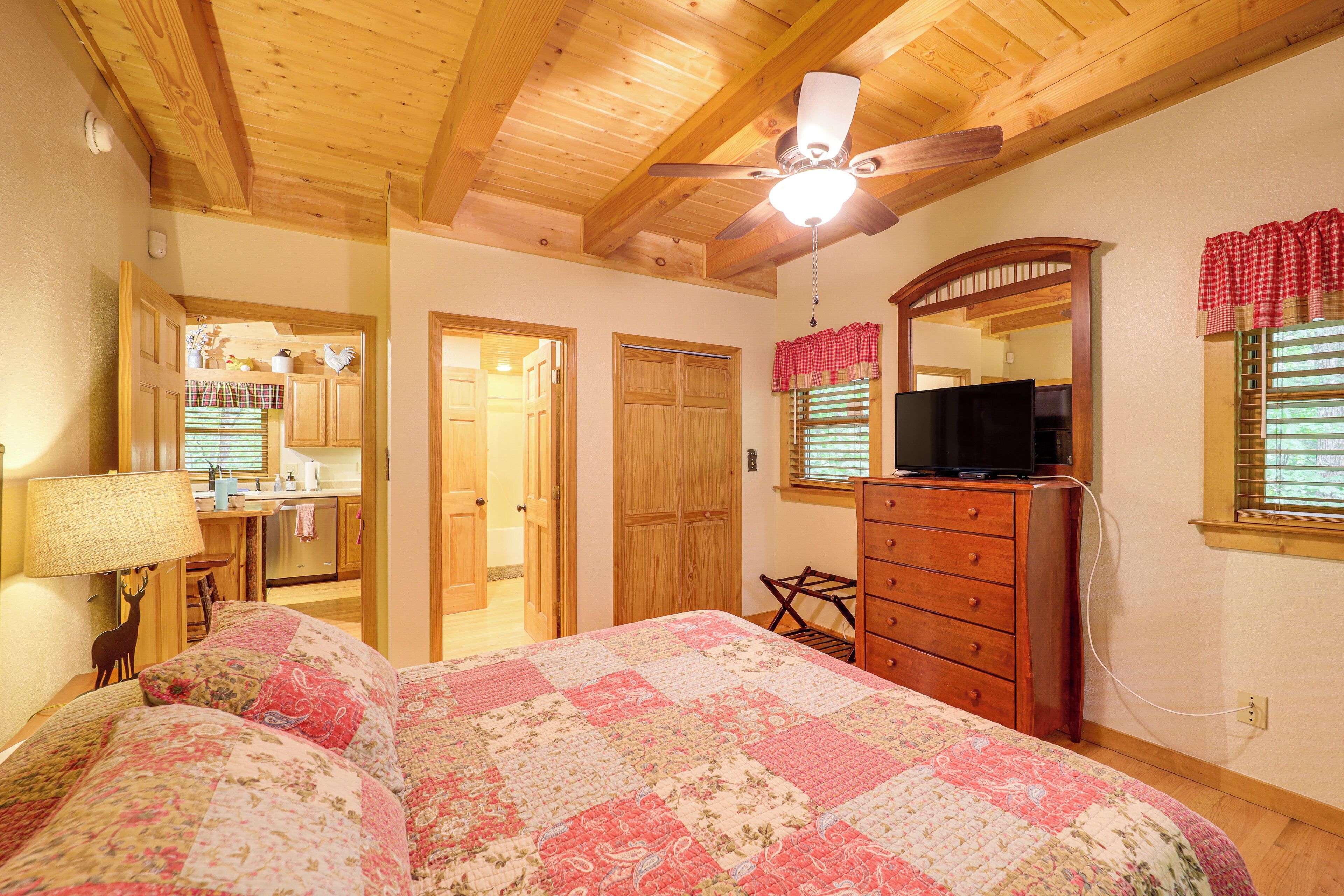 Quarto com teto de madeira, cama com colcha floral, cômoda, televisão e espelho com janela em cima.