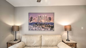 Un soggiorno con un divano beige, due tavolini con lampade e un dipinto raffigurante un panorama urbano.