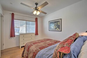 Un dormitorio con cama, ventilador de techo, ventana con cortinas, cómoda y un cuadro en la pared.