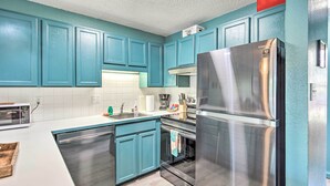 Una cucina moderna con mobili color petrolio, elettrodomestici in acciaio inossidabile e un piano di lavoro bianco.