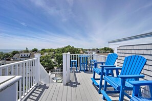 A wooden deck with blue Adirondack chairs and a white railing.