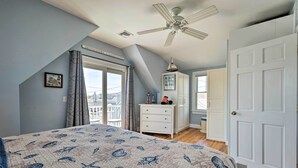 Ein Schlafzimmer mit Bett, Deckenventilator, Kommode, einer Tür und einem Fenster mit Vorhängen.