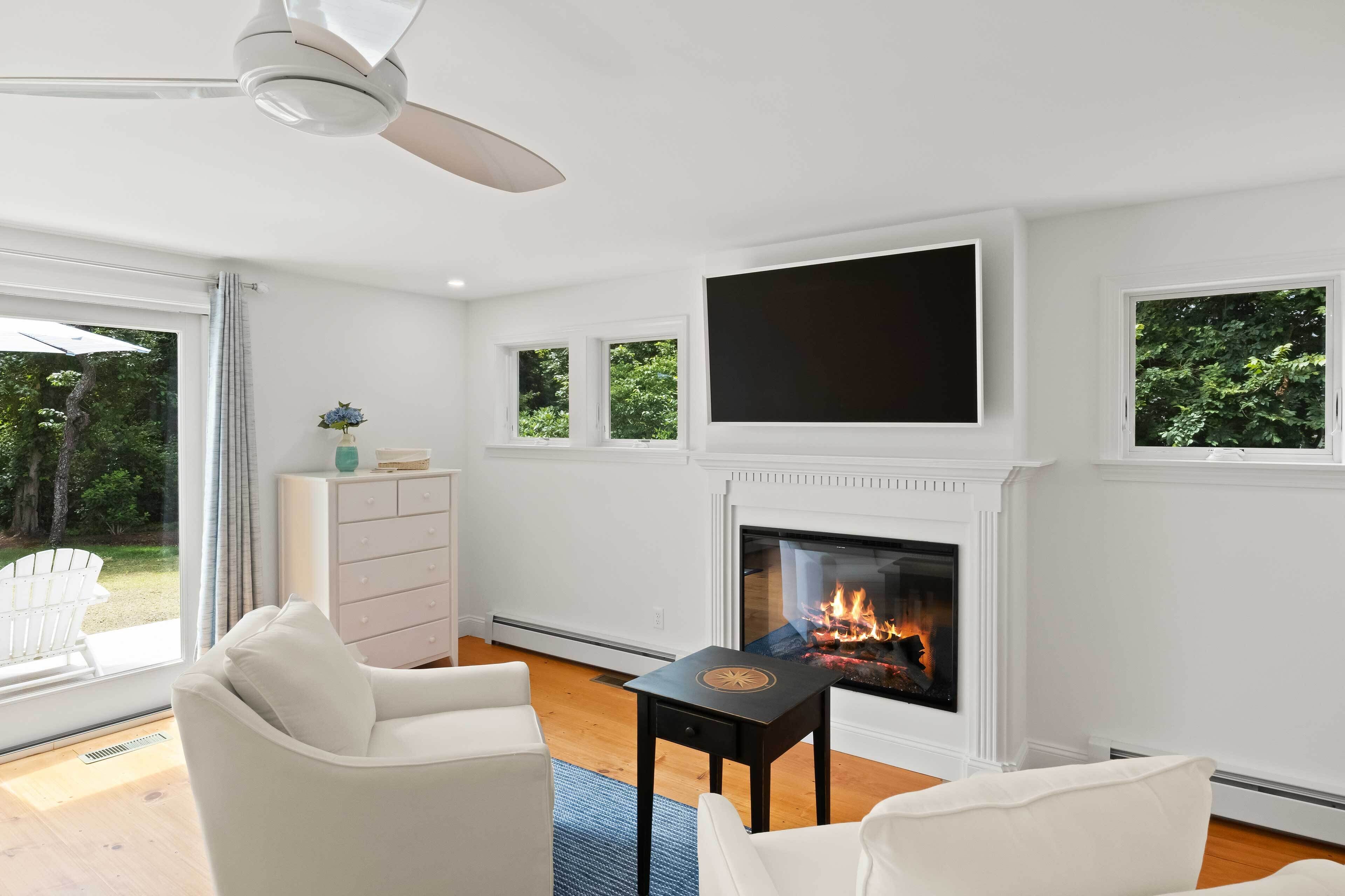 A modern living room with a fireplace, white walls, and a ceiling fan.