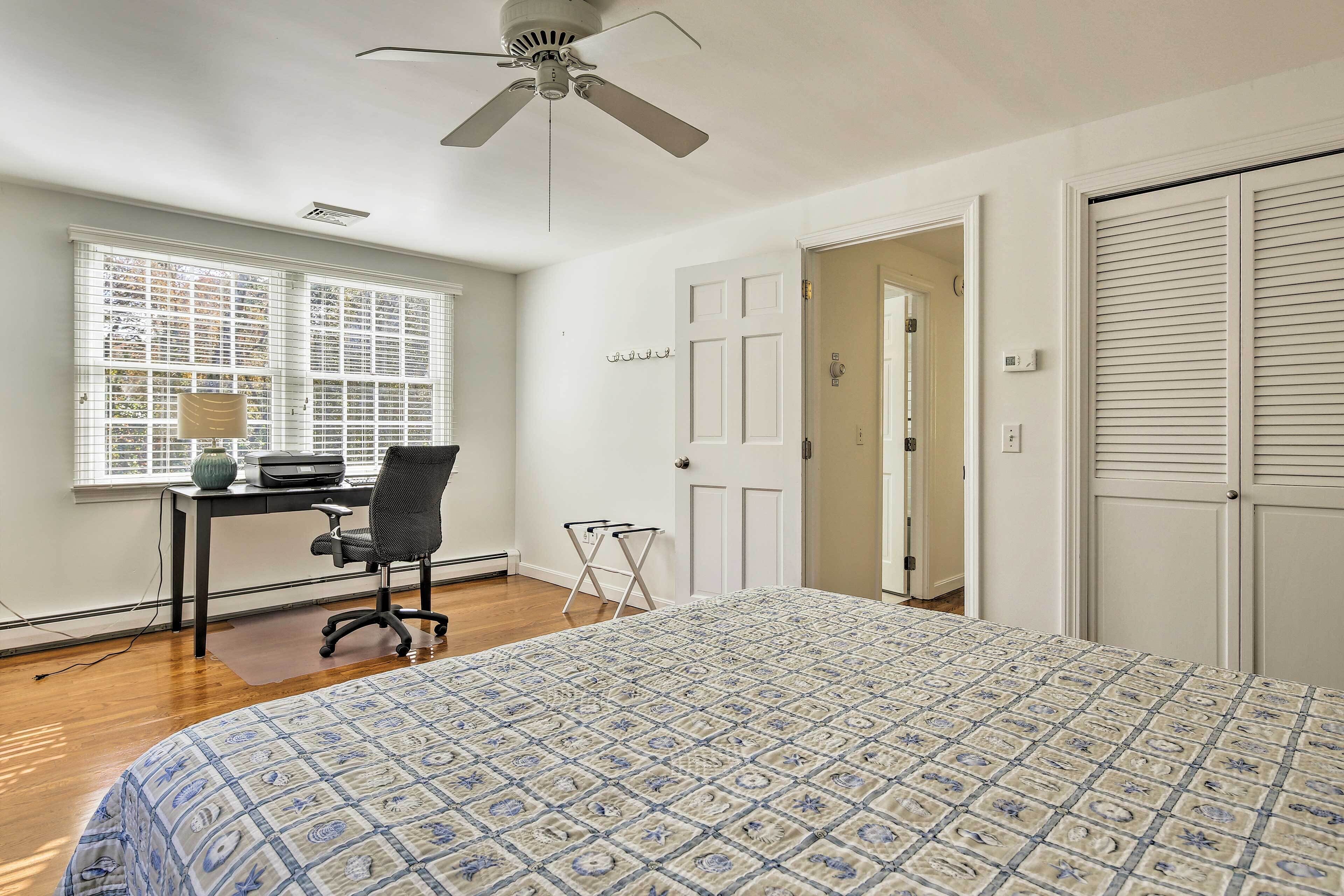 Une chambre à coucher comprenant un lit, un bureau, une chaise, un ventilateur de plafond et une fenêtre avec des stores.