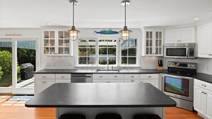 A modern kitchen with white cabinets, a large island, stainless steel appliances, and pendant lighting. - 3 Bicycles Provided! Cape Cod Cottage w/ Deck (Orleans)