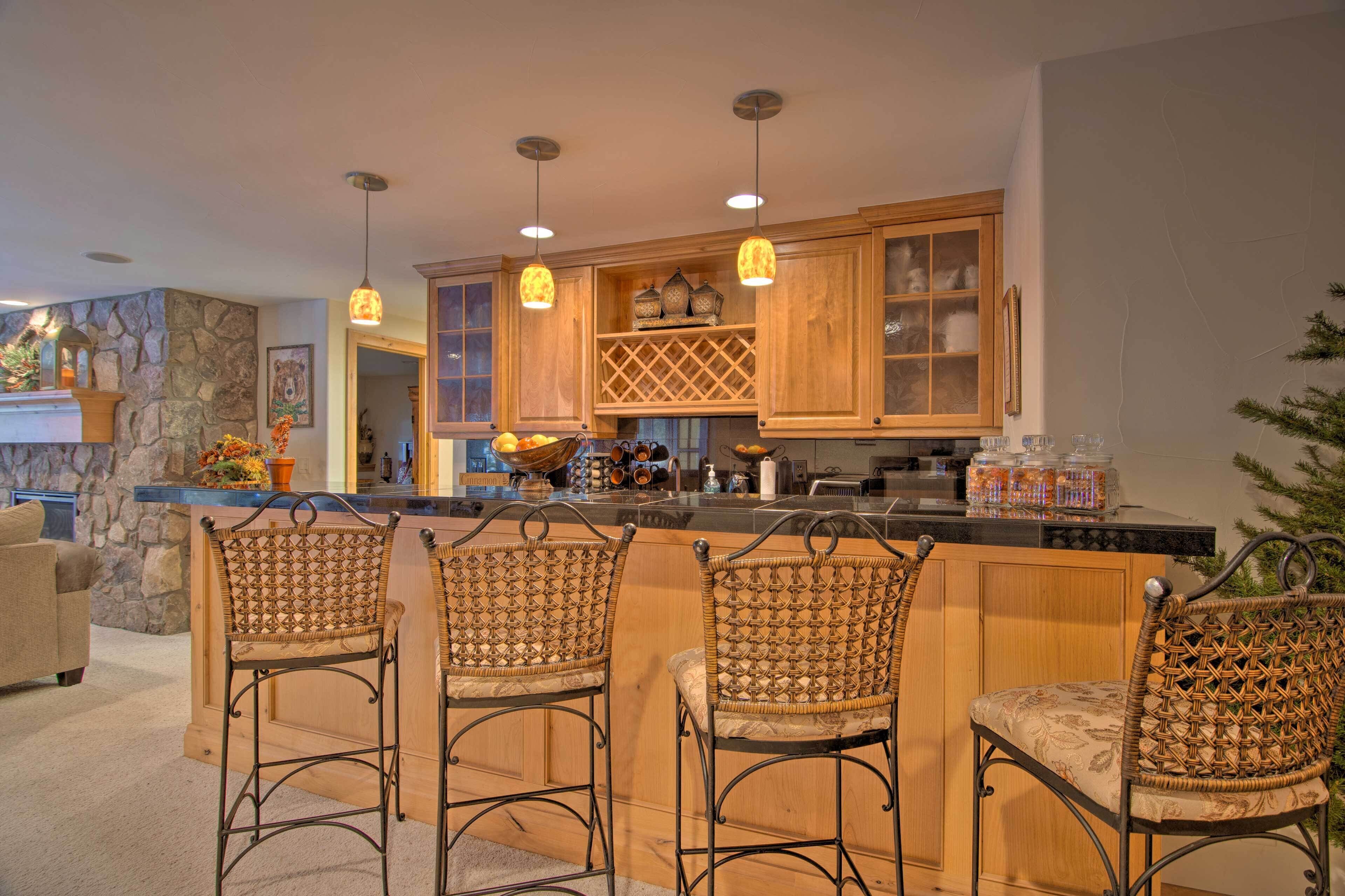 A kitchen with a stone accent wall, wooden cabinets, a bar area with wicker chairs, pendant lighting, and a fruit bowl.