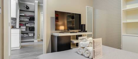A hotel room with a bed, a desk with a mirror, a TV, and a walk-in closet.
