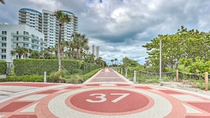 A paved pathway with a red and white pattern, leading towards a modern high-rise building. - Sunny Miami Beach Condo Steps to Boardwalk! (Miami Beach)