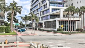 A modern multi-story building with balconies, palm trees, and a clear sky. - Sunny Miami Beach Condo Steps to Boardwalk! (Miami Beach)
