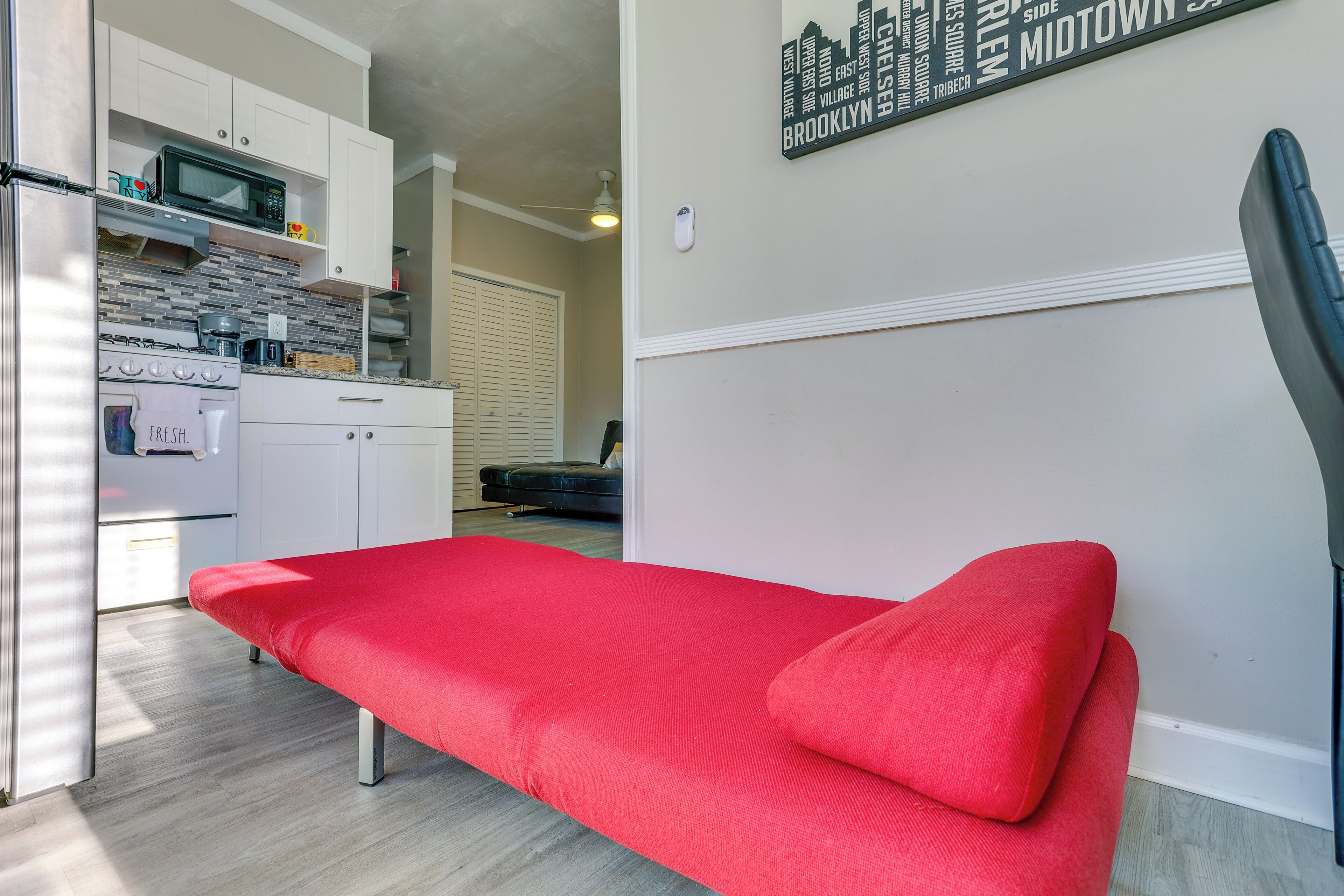 Un espacio habitable compacto con kitchenette, un sofá rojo y un letrero de paisaje urbano colgado en la pared.