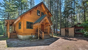 A wooden cabin with a porch, a small attached structure, and a gravel driveway. - Secluded Leavenworth Cabin on Chiwawa River! (Leavenworth)