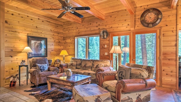 A cozy log cabin interior with a fireplace, leather furniture, and large windows offering a view of the forest. - Secluded Leavenworth Cabin on Chiwawa River! (Leavenworth)
