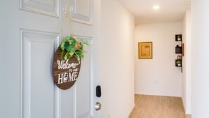 A hallway with a welcome sign, a framed picture on the wall, and a small shelf with decorative items. - Cozy Texas Escape Near Seaworld San Antonio! (San Antonio)