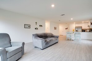 A modern living room with a grey sofa, a white dining table with chairs, and a kitchen area with white cabinets and a refrigerator. - Cozy Texas Escape Near Seaworld San Antonio! (San Antonio)
