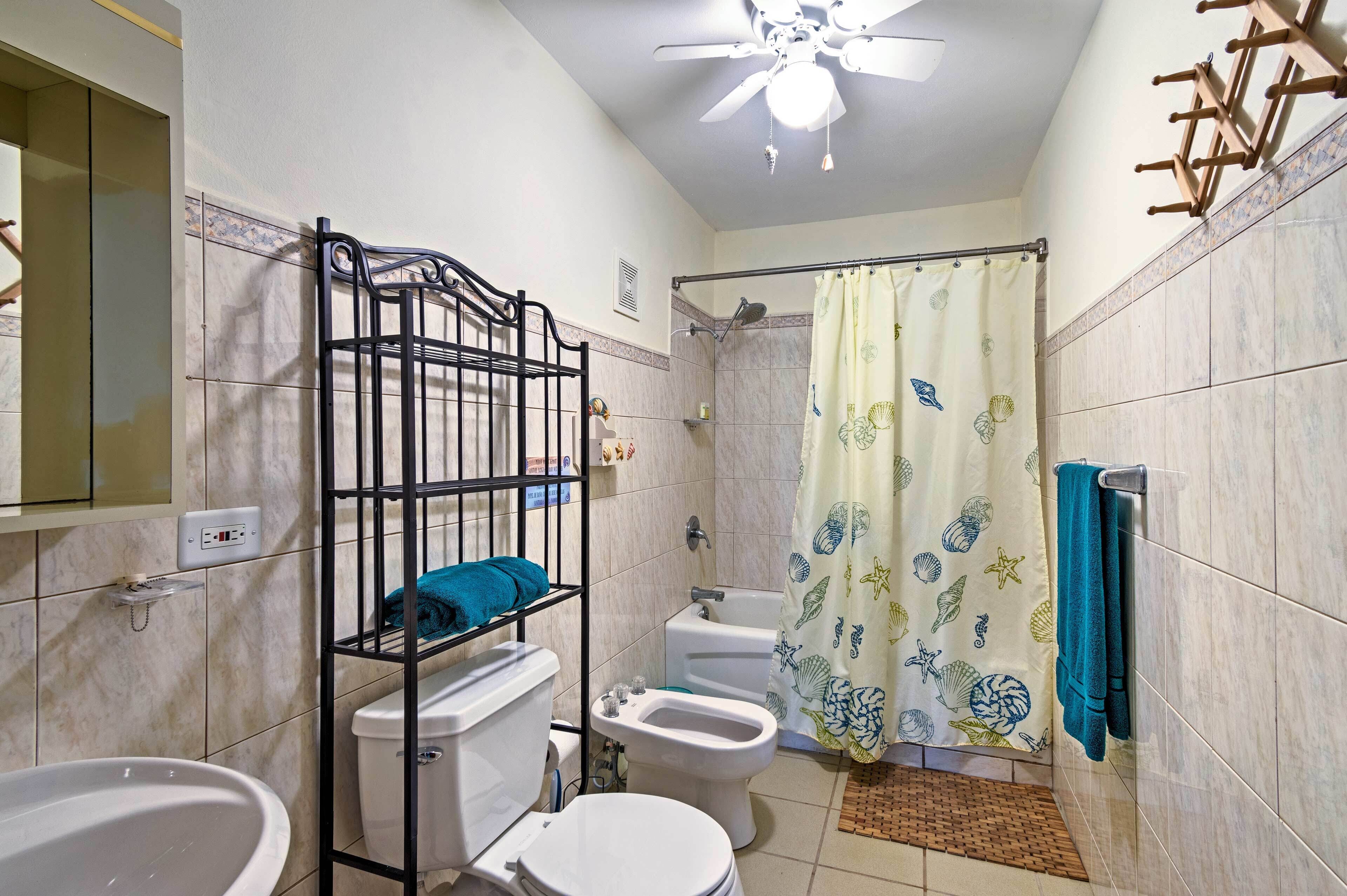 A bathroom with a toilet, bidet, bathtub, and a shower curtain with a sea theme.