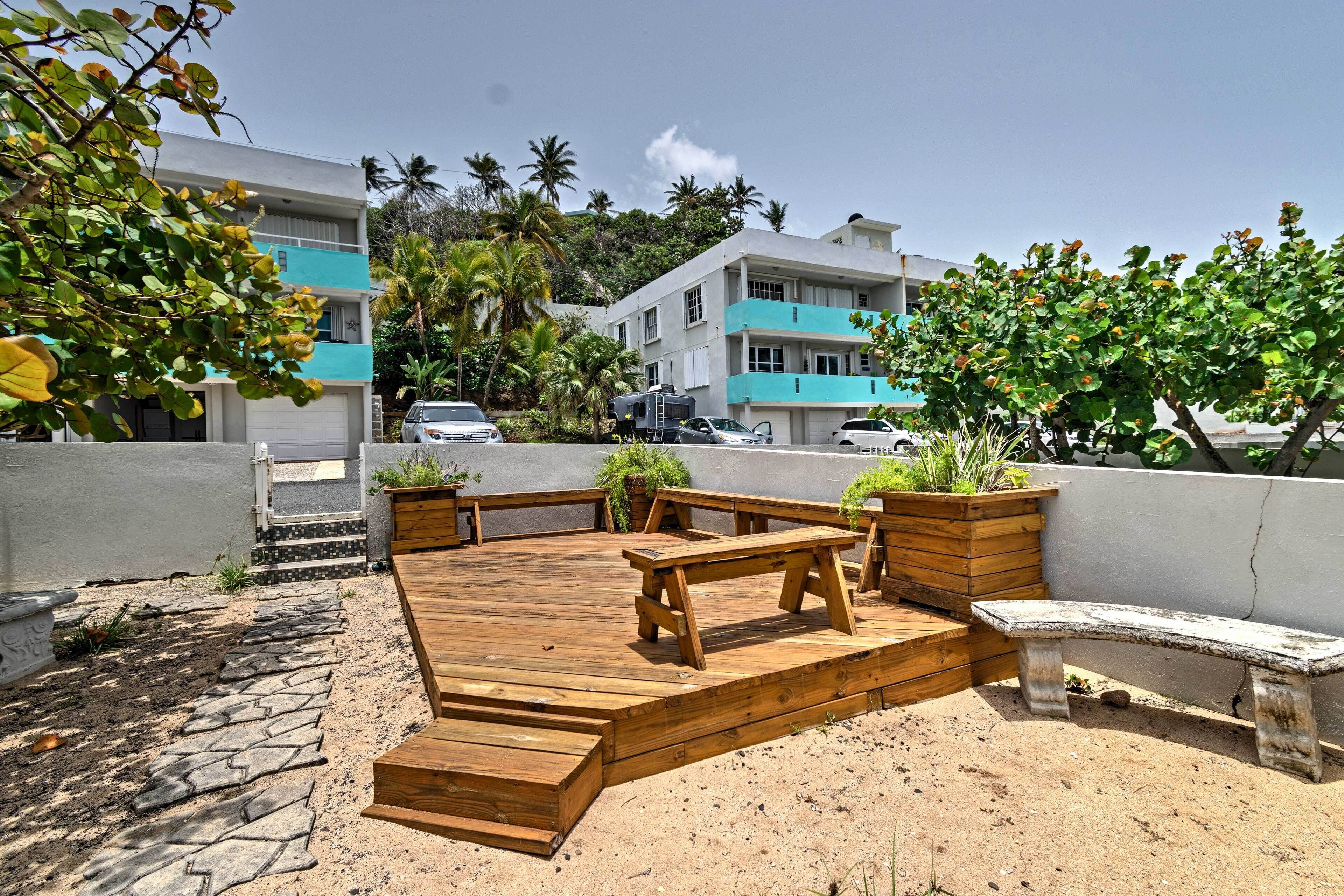 A wooden deck with benches and planters, surrounded by a white wall and palm trees.