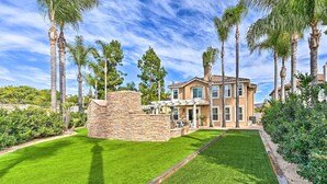 A two-story house with a stone patio, surrounded by a well-maintained lawn and tall palm trees. - Stunning Carlsbad Gem w/ Fire Pit & Hot Tub! (Carlsbad)