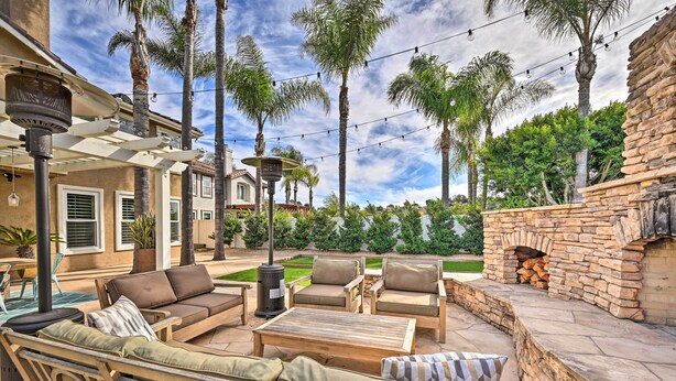 An outdoor patio area with a stone fireplace, outdoor furniture, and string lights. - Stunning Carlsbad Gem w/ Fire Pit & Hot Tub! (Carlsbad)