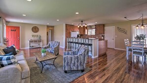 A spacious living room with a sofa, armchairs, and a coffee table. A kitchen with wooden cabinets and a dining area with chairs is visible in the background. - Ellensburg Home w/ Mountain Views on 3 Acres! (Ellensburg)