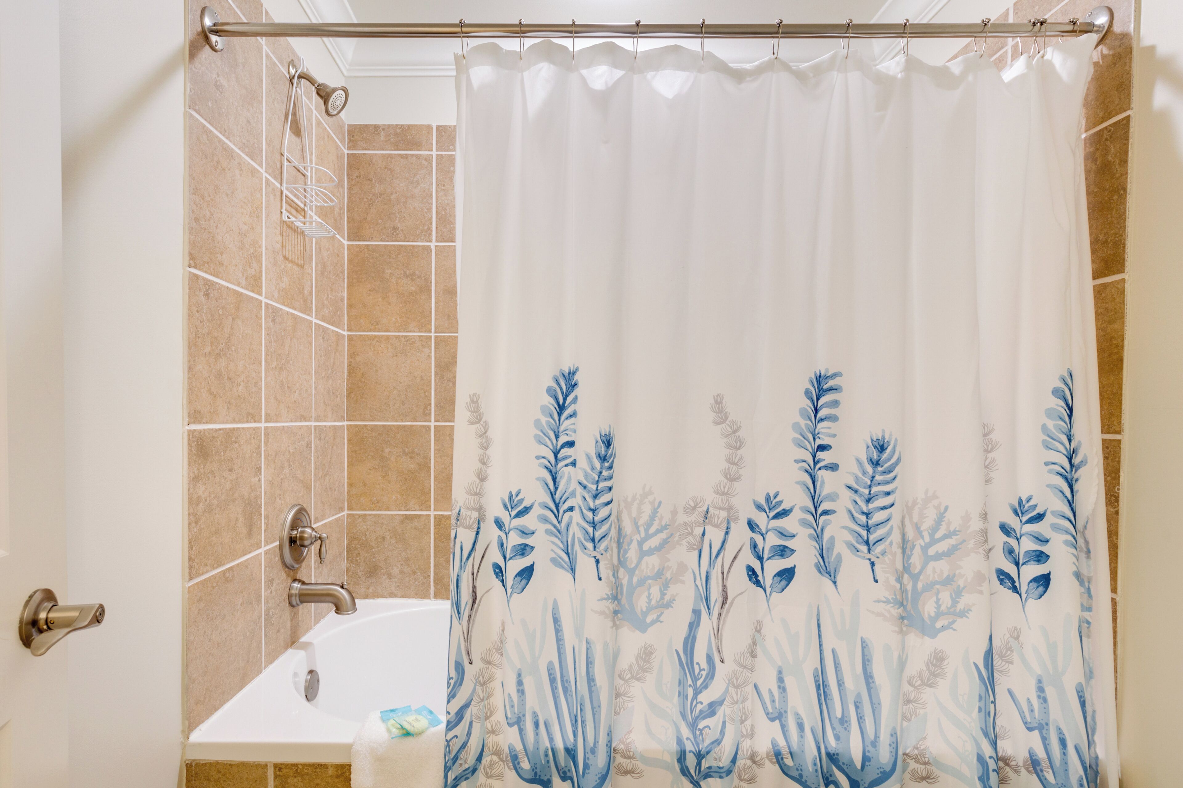 Un baño con cortina de ducha con diseño acuático azul, una bañera blanca y un cabezal de ducha.