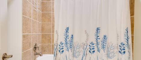 Un baño con cortina de ducha con diseño acuático azul, una bañera blanca y un cabezal de ducha.