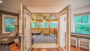 A cozy room with a wooden floor, a sofa, a chair, and a dining table. There are large windows with a view of trees. - Peaceful Forest Retreat by Mt. Baker Slopes! (Deming)