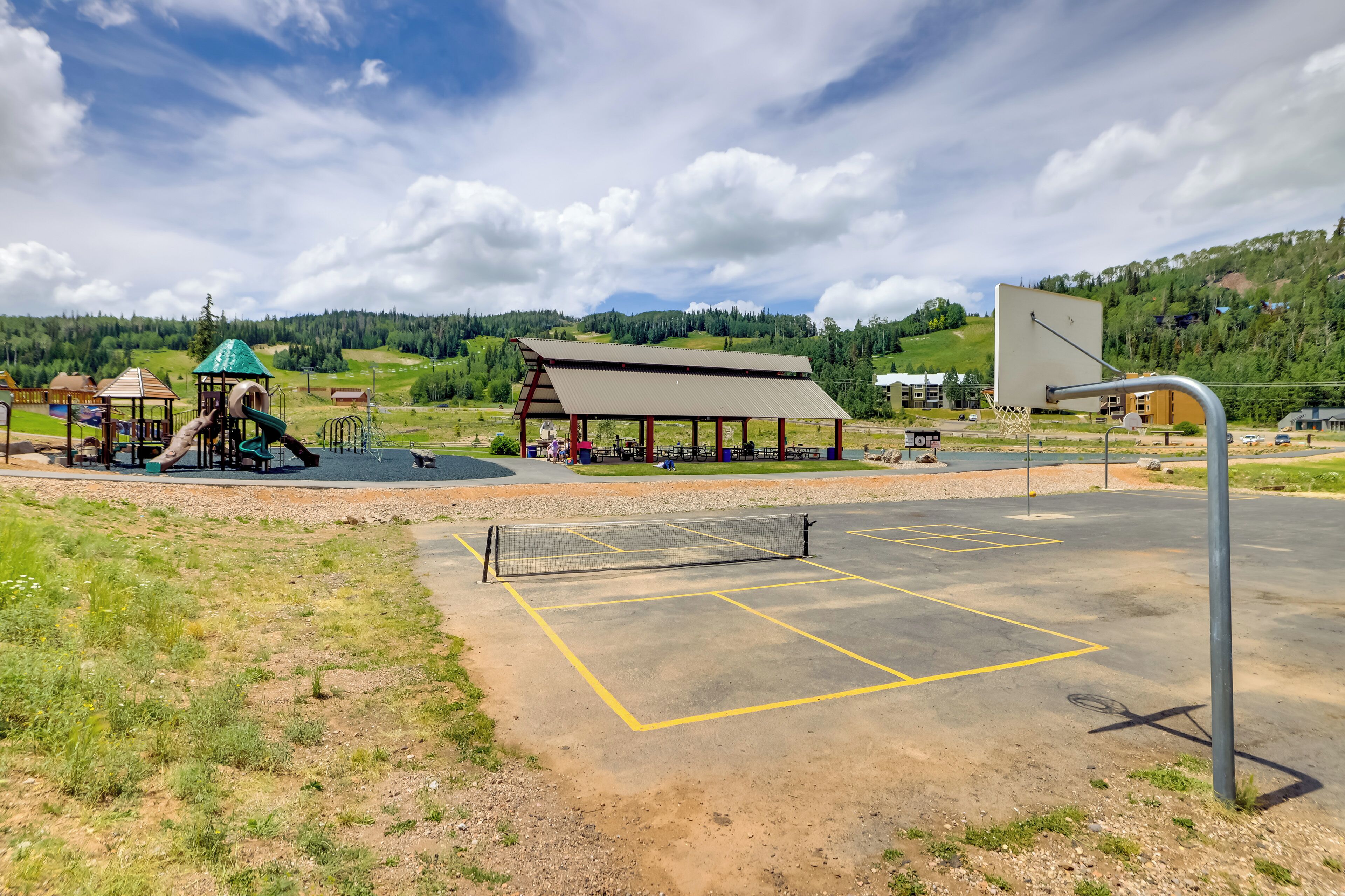 An outdoor sports court with a basketball hoop and a playground area with slides and swings.