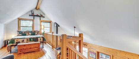 Une pièce aux hauts plafonds, dotée d’un plancher en bois, d’un lit recouvert d’une couvre-lit à motifs verts et blancs, d’un banc en bois et d’un escalier menant à un niveau supérieur.