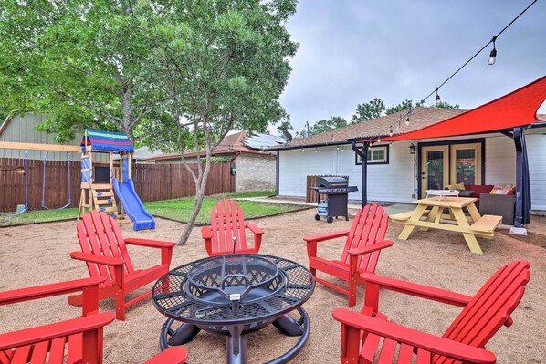 A backyard with a playset, red Adirondack chairs, a fire pit, and a picnic table. - San Antonio Family Home w/ Game Room & Fire Pit! (San Antonio)