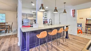 A modern kitchen with a central island, pendant lighting, and a retro arcade sign. - San Antonio Family Home w/ Game Room & Fire Pit! (San Antonio)