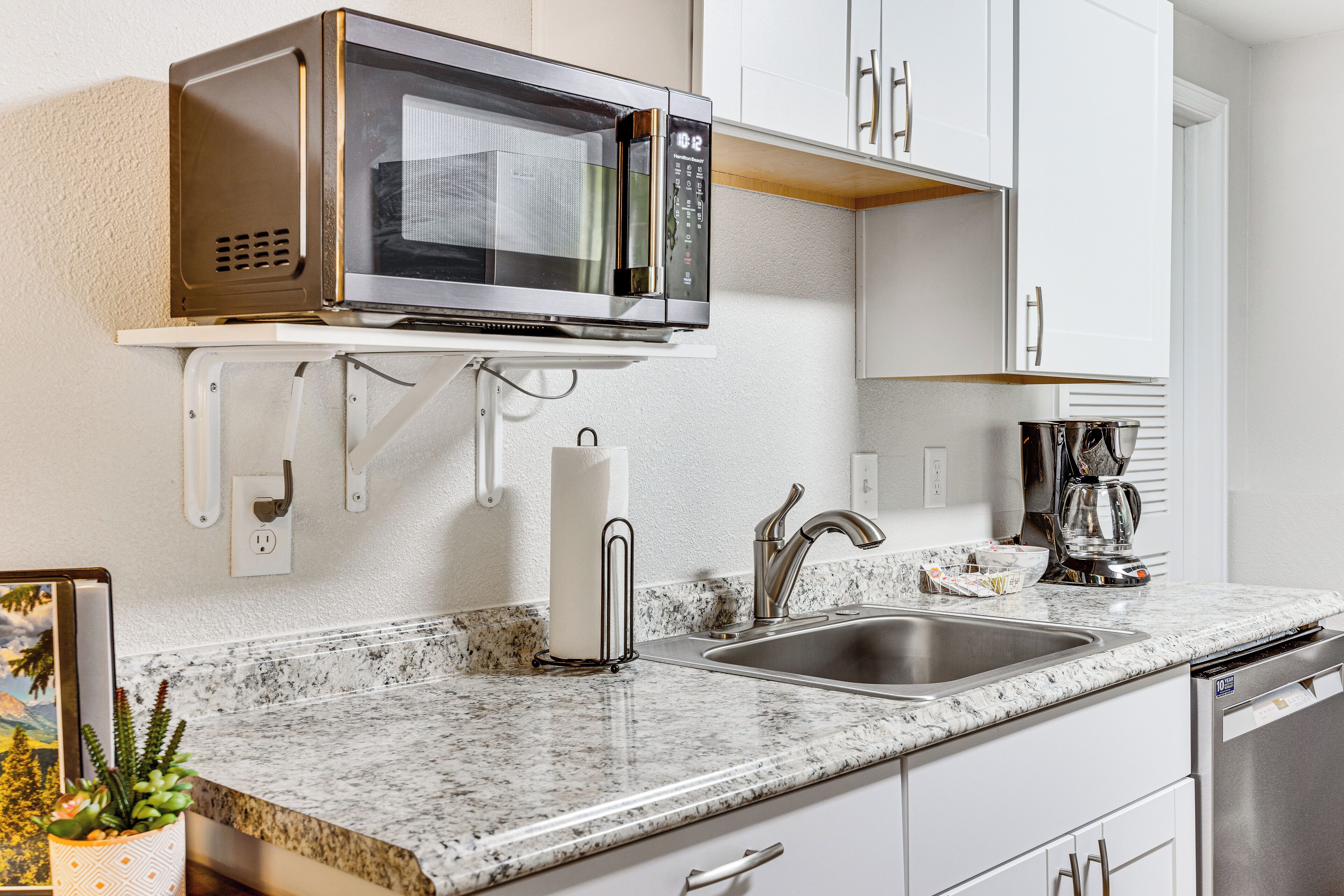 A kitchen with a built-in microwave, a stainless steel sink, and white cabinetry.