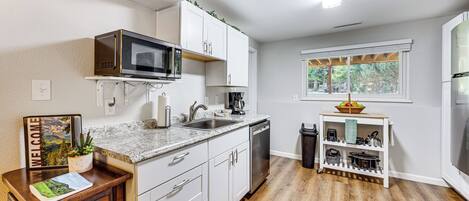 A modern kitchen with white cabinets, a built-in microwave, a sink, and a wooden floor.