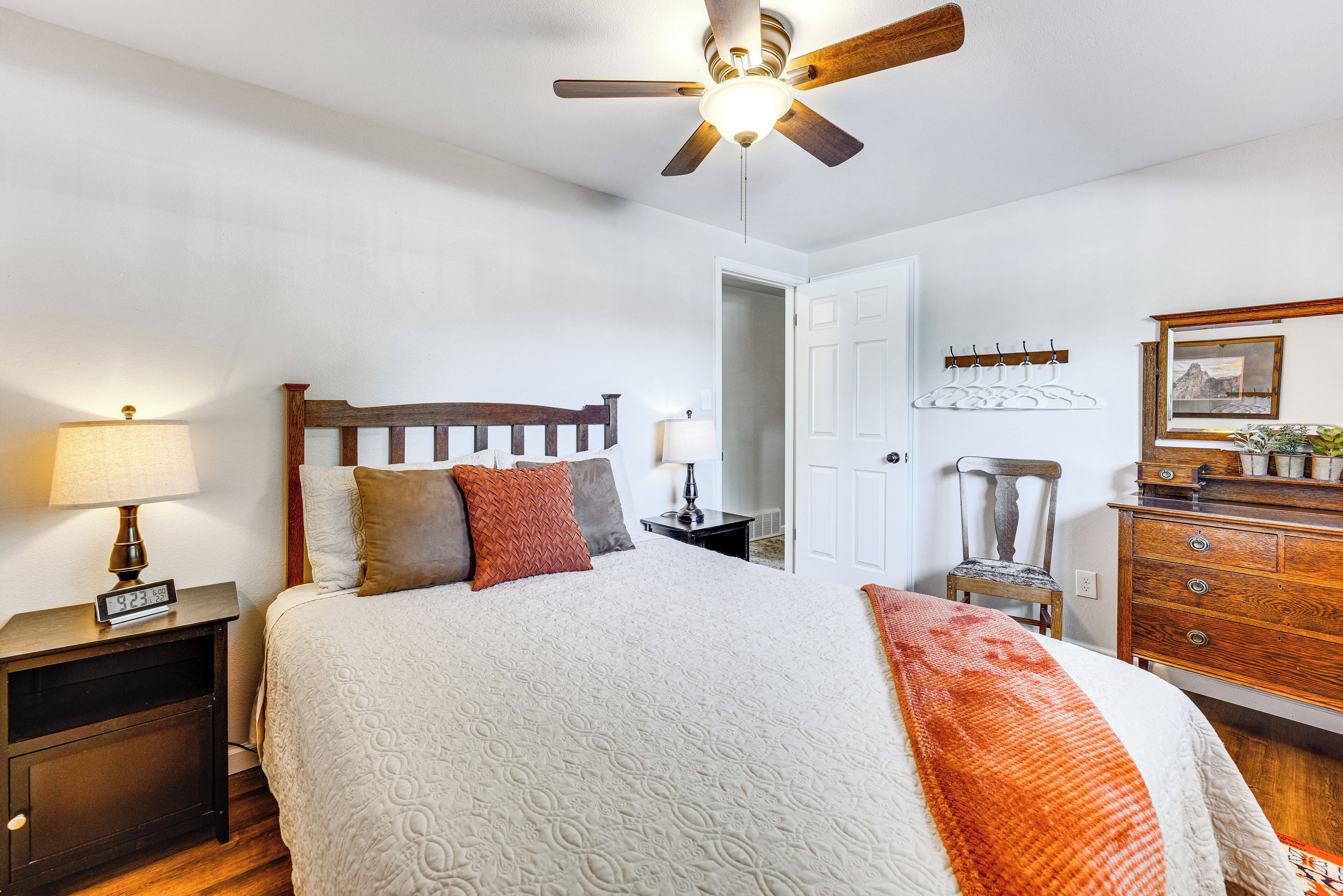 A bedroom with a bed, a nightstand with a lamp, a dresser, a ceiling fan, and a door.