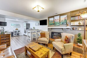 A modern living room with a fireplace, comfortable seating, and a bookshelf. - Hillside Place w/ Mountain Views ~ 8 Mi to Dtwn! (Colorado Springs)